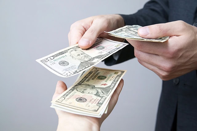 10 Financial Mistakes to Avoid Entering Retirement 8 a person handing cash to another person.