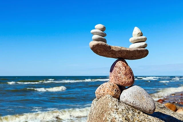 two piles of rocks are perfectly balanced on a long rock that itself is balanced on another rock.